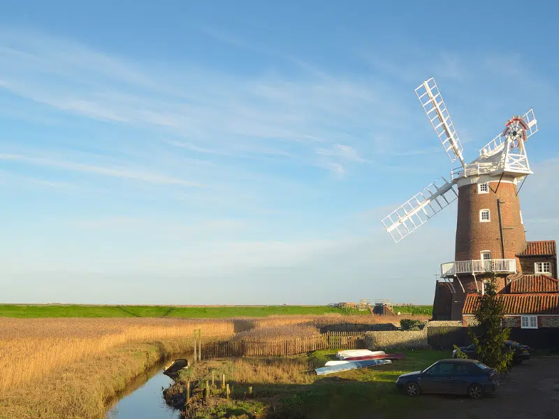 Red brick windmill with white sails overlooking reed beds and marshes