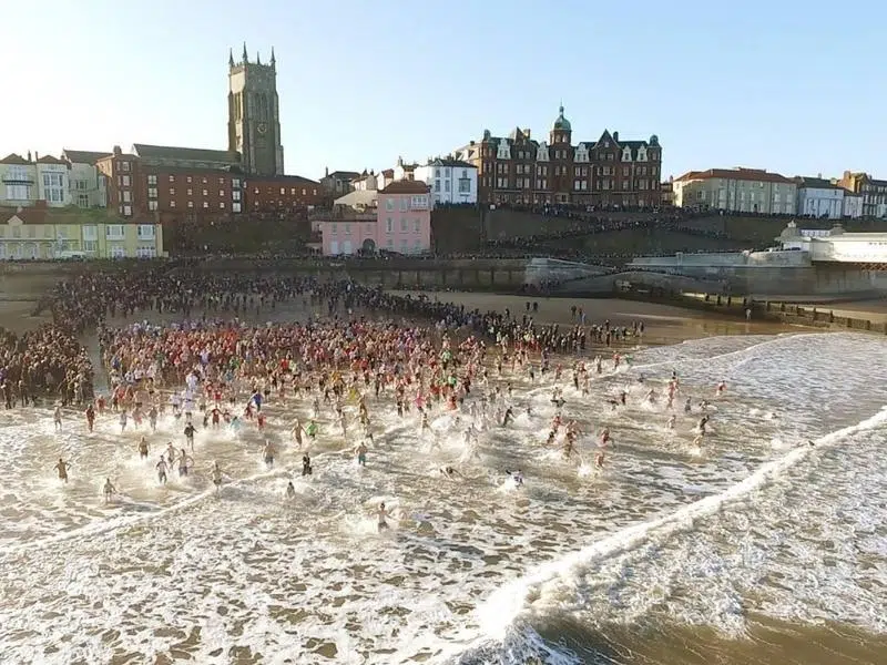 large group of people running into the North Sea in winter from a beach