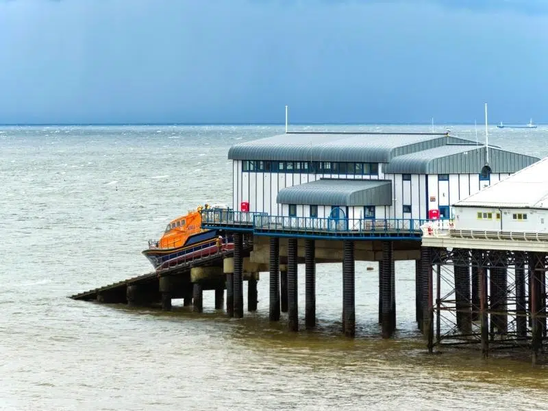 orange lifeboat being launched into the sea from the end of a pier