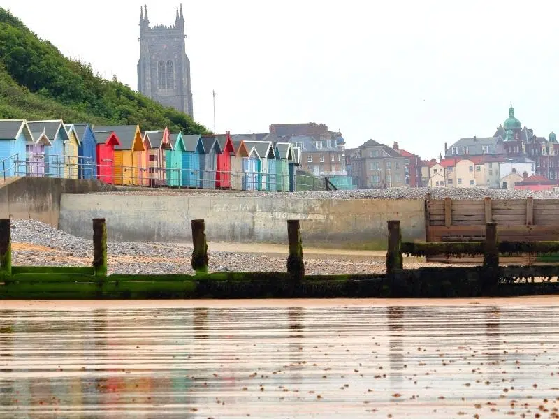 brightly painted beach huts with a church in the background and shingle beach in the foreground