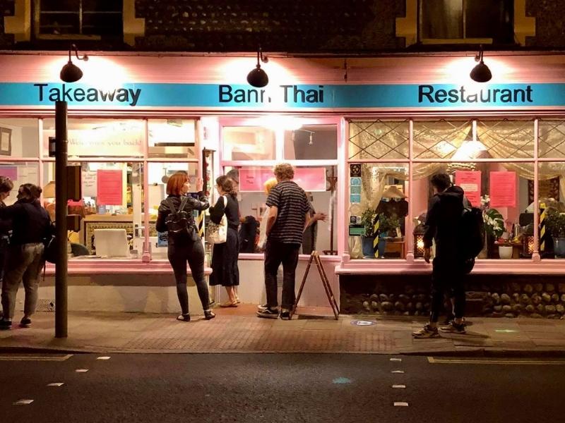 Pink and blue restaurant lit up at night, with people outside