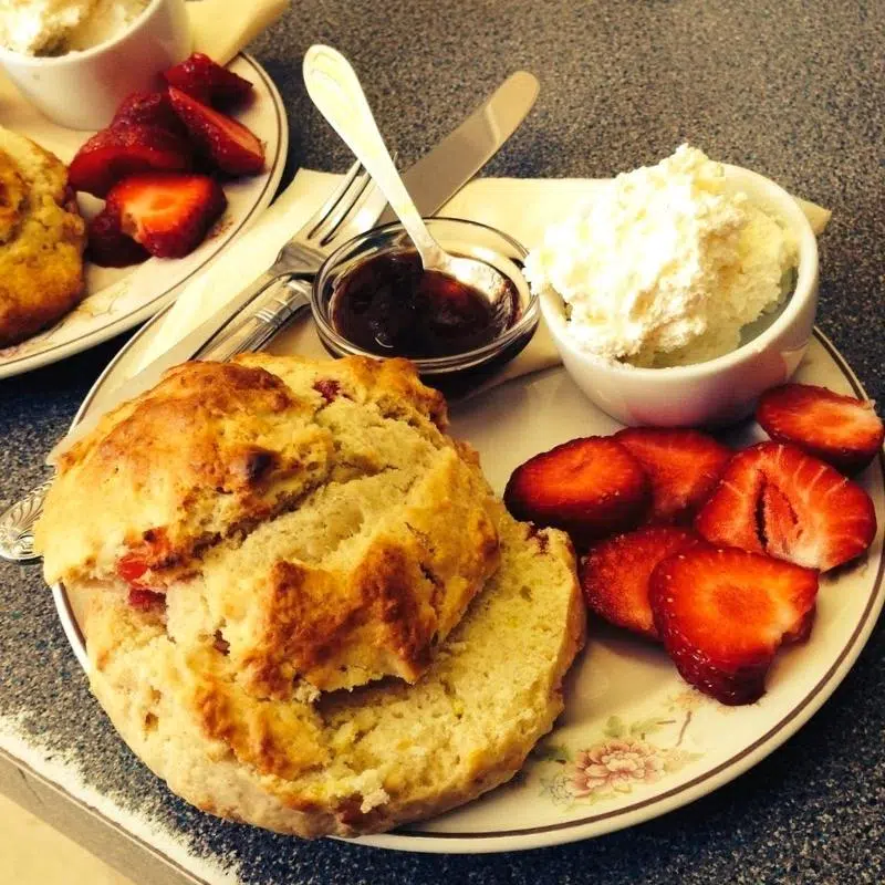 Scone on a plate with fresh strawberries, strawberry jam and clotted cream