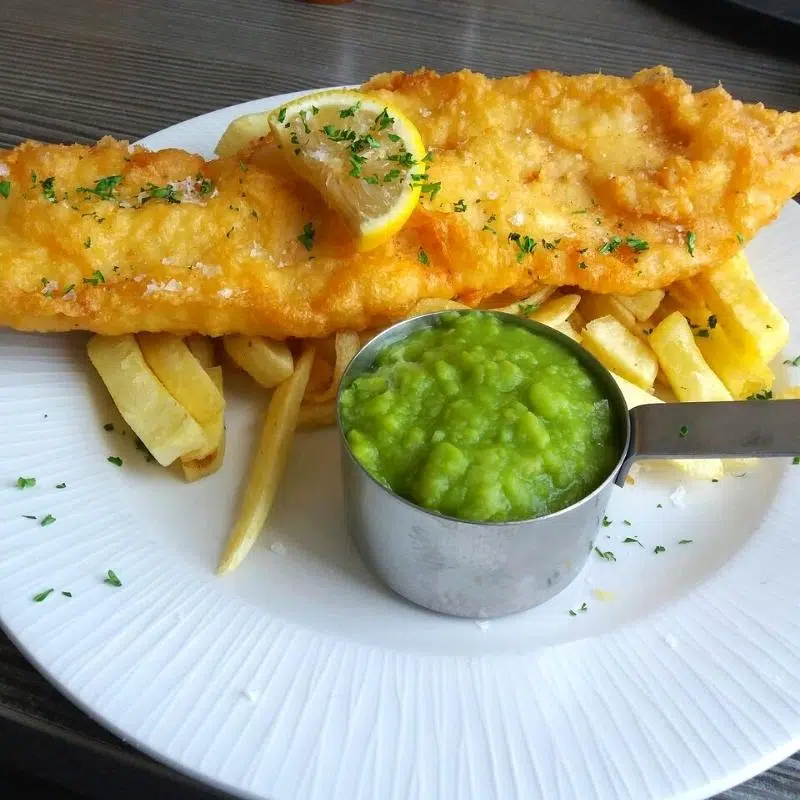 fish, chips and mushy peas served with a slice of lemon and parsley on a white china plate