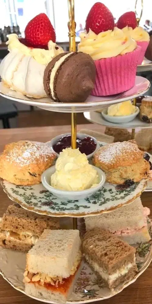 Cake stand displaying sandwiches, scones, jam, cream, cupcakes and macaroons
