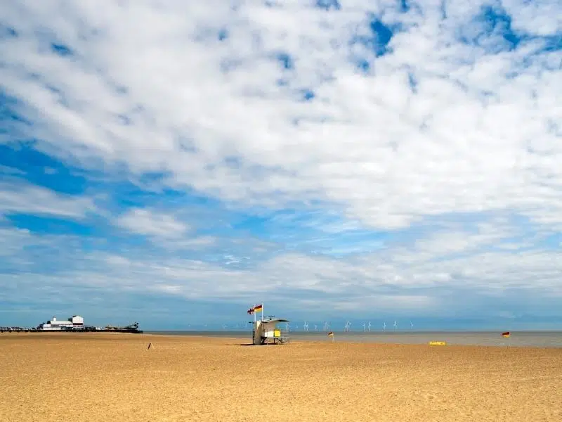 wide sandy beach with lifeguard hut and funfair and off shore wind turbines in the background