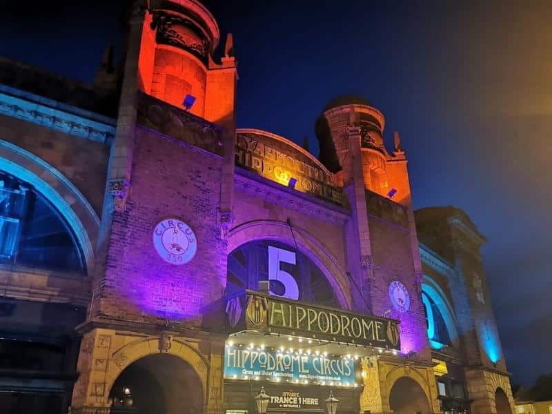 Front of large theatre building with turrets, lit with red and purple lights at night