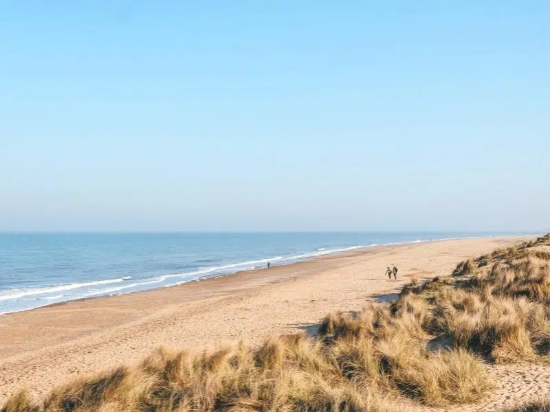 long sandy beach with three people walking by the sea