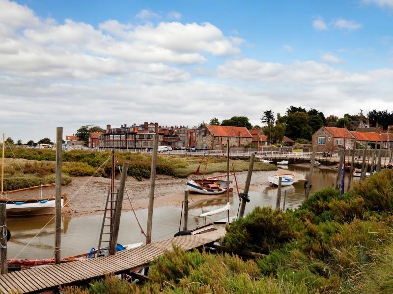 Tidal creek with wooden boardwalk small boats backed by orange roofed cottages