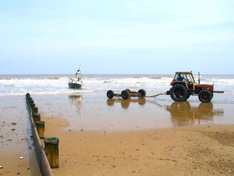 tractor waiting for small boat to land on sandy beach