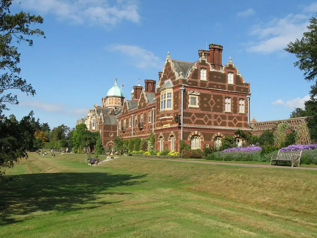 Red brick Edwardian stately home facing colourful gardens and trees with blue sky