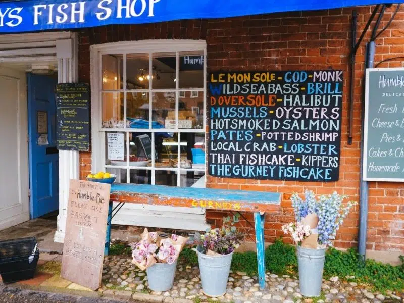 a small shop with blue awning and white 16 pane window, with a chalkboard advertising seafood for sale