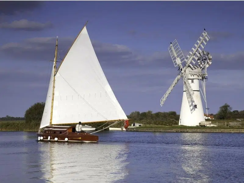 Boat with white sails sailing past Thurne Mill