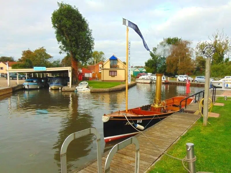 small red sailing vessell with chomney on a Norfolk Broad