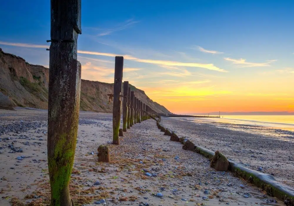 sand and pebble beach at sunset with long line of groins and cliffs behind