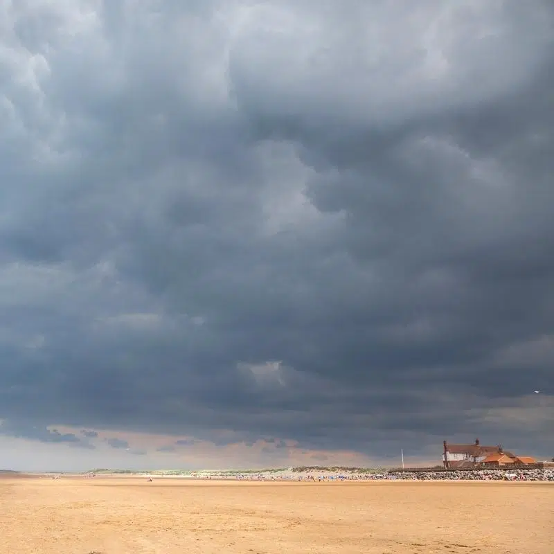 huge sandy beach with buildings and people in the distance, under a dark grey cloudy sky