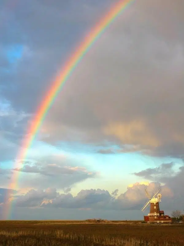 red brick windmill with white cap and sails underneath a rainbow