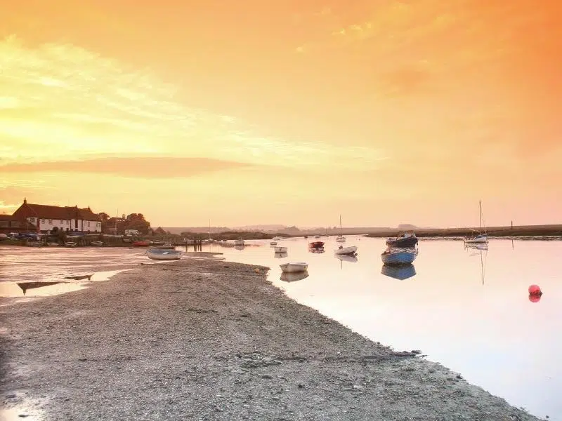 boats bobbing at sunset in tidal waters along mud flats with a white building in the background