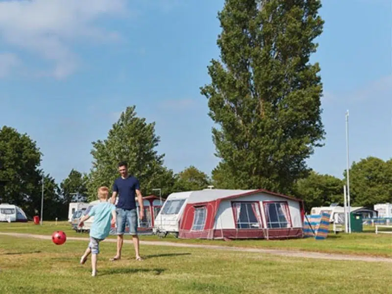 Man and child playing football in front of large caravan and red awning