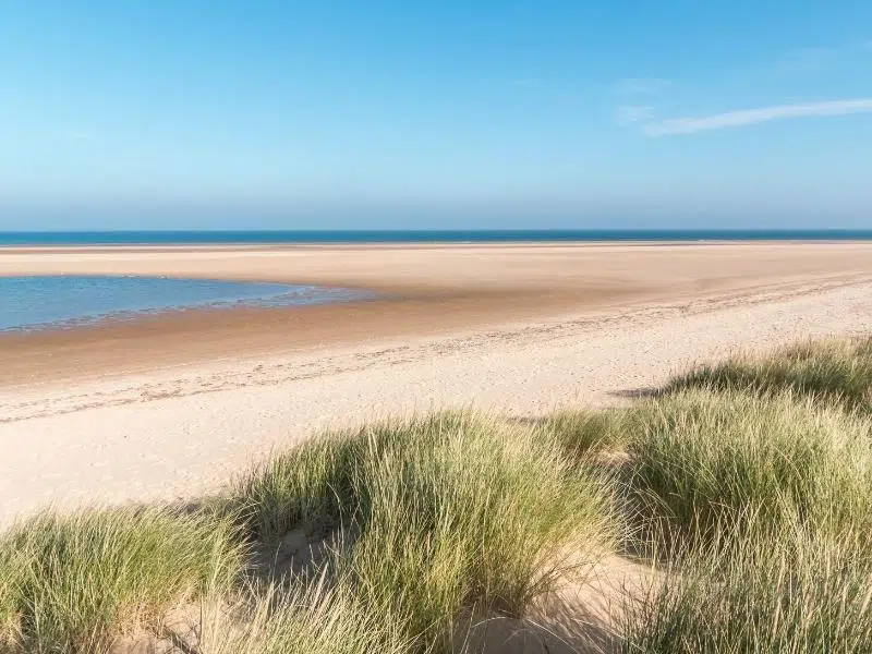Large expanse of sandy beach with a blue sea and marram grass covered sand dunes