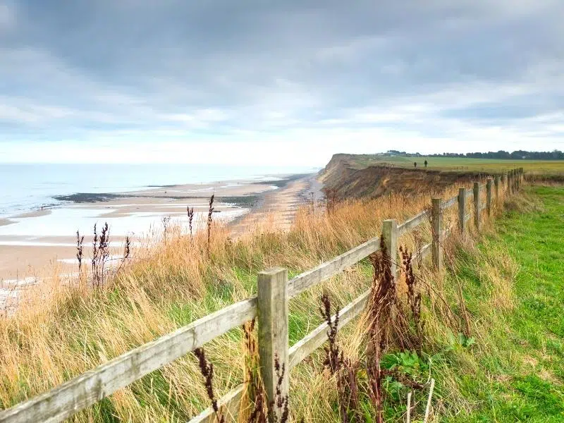 View of West Runton beach and cliffs over a wooden fence