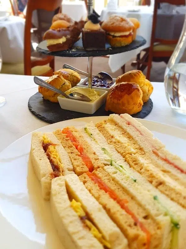 finger sandwiches arranged on a plate and cake stanf with scones, jam and cream