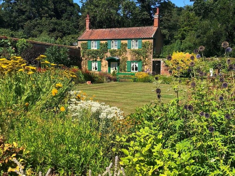 Gardens at Hoveton Hall with a small cottage with green shutters and red tiled roof in the background