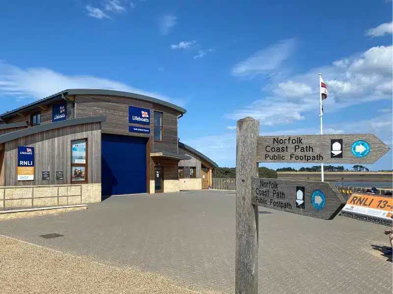 wood, brick and metal lifeboat station with a Norfolk Coast Path sign