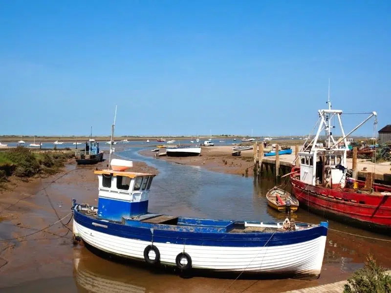 Red, blue and white fishing vessels in small harbour with the tide out