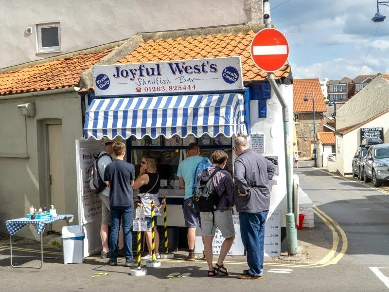 Shellfish hut with blue and white striped canopy, and people waiting to be served