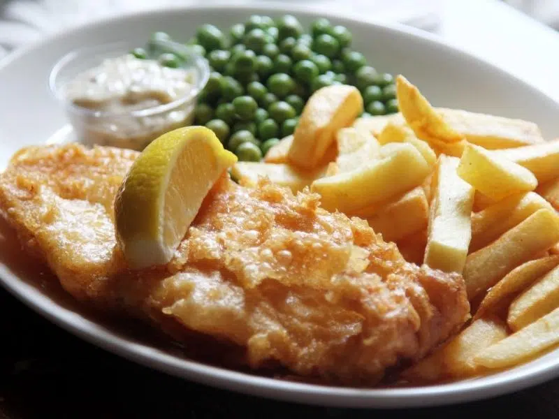 battered fish, chips and peas with tartar sauce and a lemon wedge