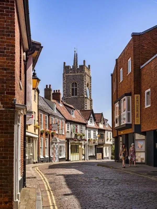 pretty cobbled street with brick and flint church in the background