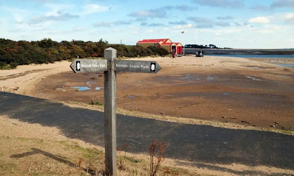 Norfolk coast path sign on the beach with Wells lifeboat station and the pine woods in the background