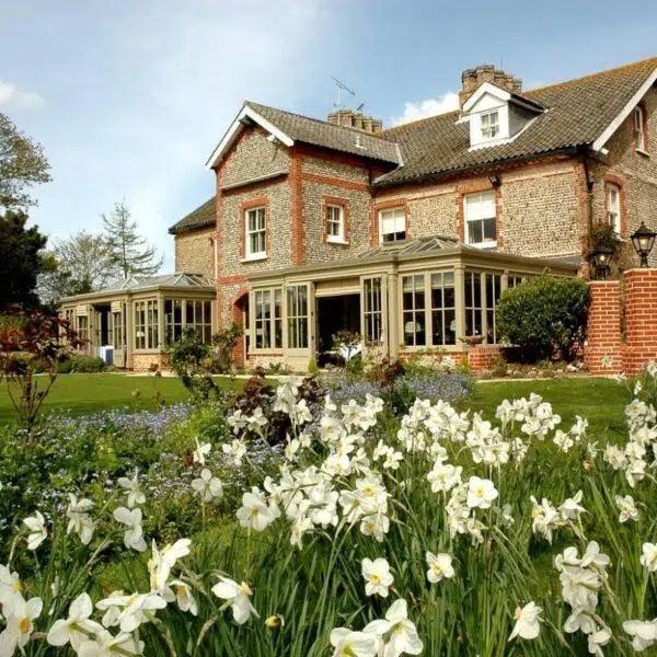 An image of the back of a hotel with its doos open to a garden filled with white flowers