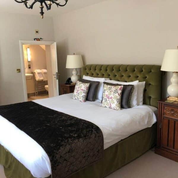 An image of a bedroom with a green headboard and throw pillows, with a door ajar to the bathroom