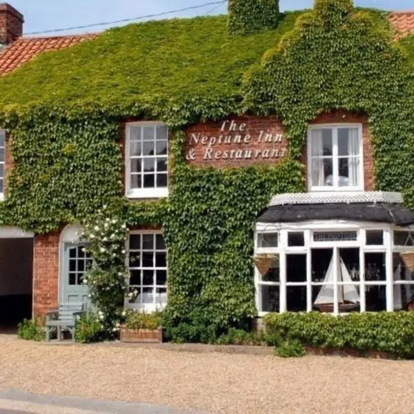 An image of the front of the Neptune hotel, an old Victorian cottage with a bay window, it is covered in Ivy
