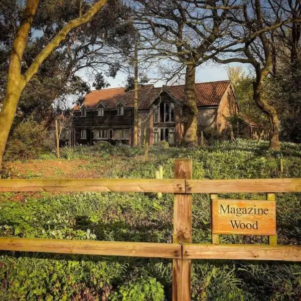 An image of an house in a meadow with trees and a wooden fence with a wood sign saying Magazine Wood