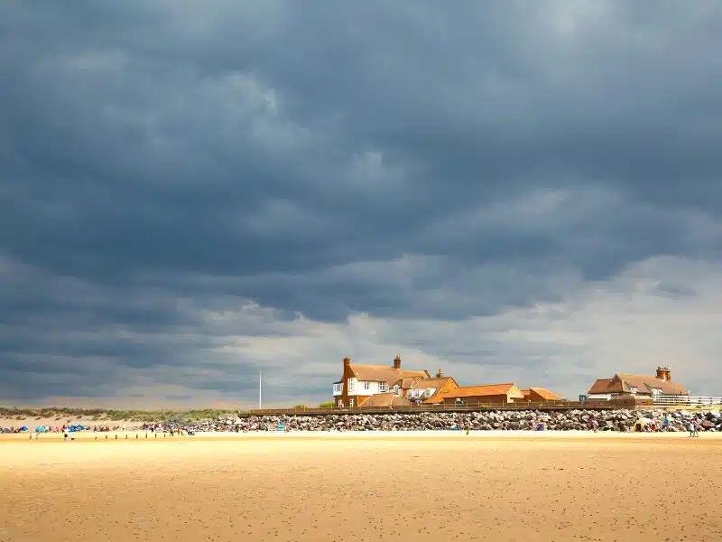 Large expanse of sand which brown and white building and a grey sky