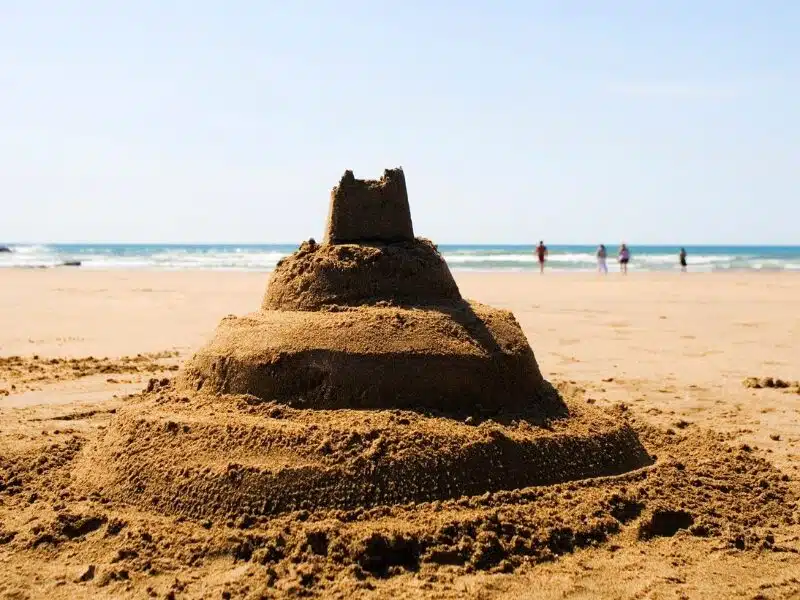 Four tiered sandcastle with people and the sea in the background