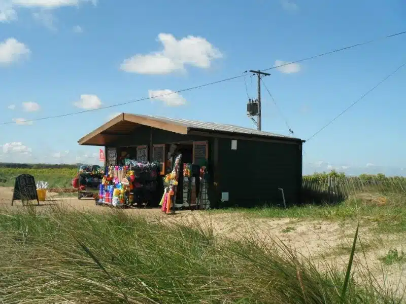 Large beach hut in graddy dunes with selection of beach toys and windbreaks on display outside