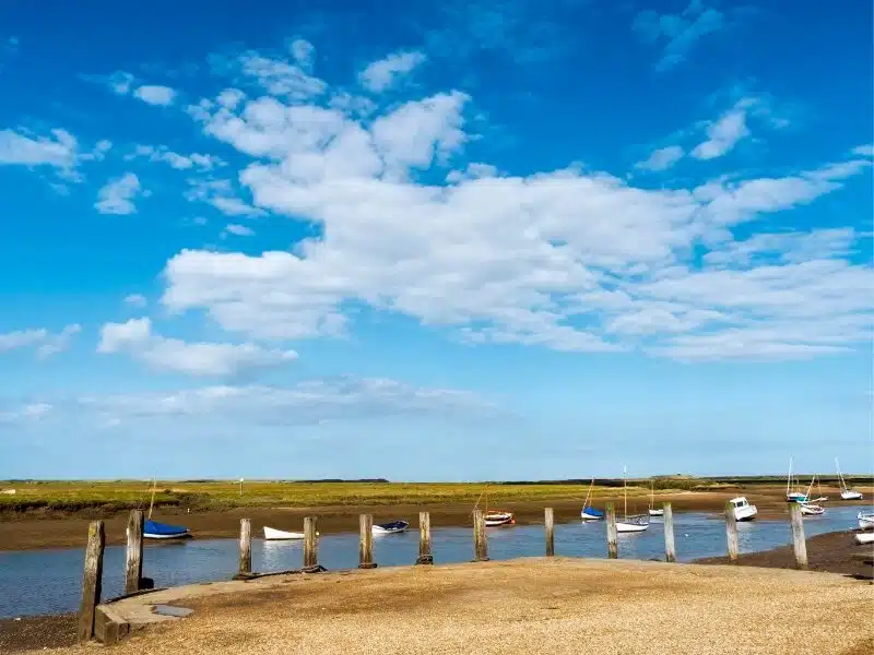 a jetty lined wuth wooden posts and colourful boats in the distance