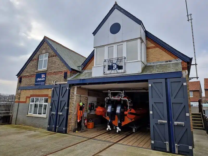 Lifeboat station with blue doors open and an orange lifeboat displayed