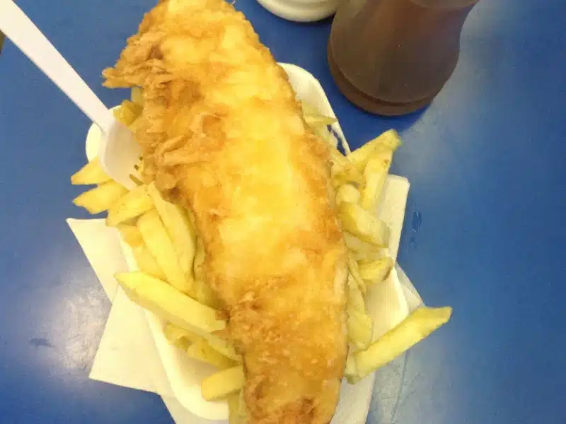 Battered fish and chips with a plastic fork, served in a polystyrene tray