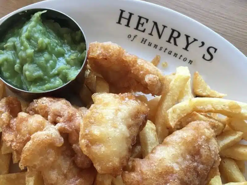 Fish and chips served with mushy peas in a metal container, on a white plate