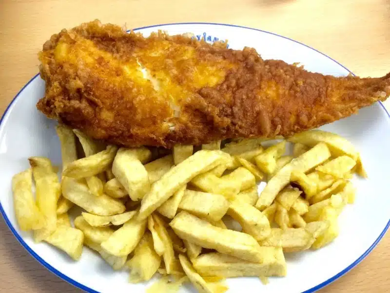 Crispy battered haddock and chips on a white plate with blue edging