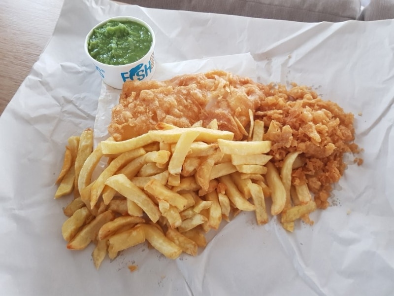 Fish, chips, scraps and mushy peas served in white chip paper