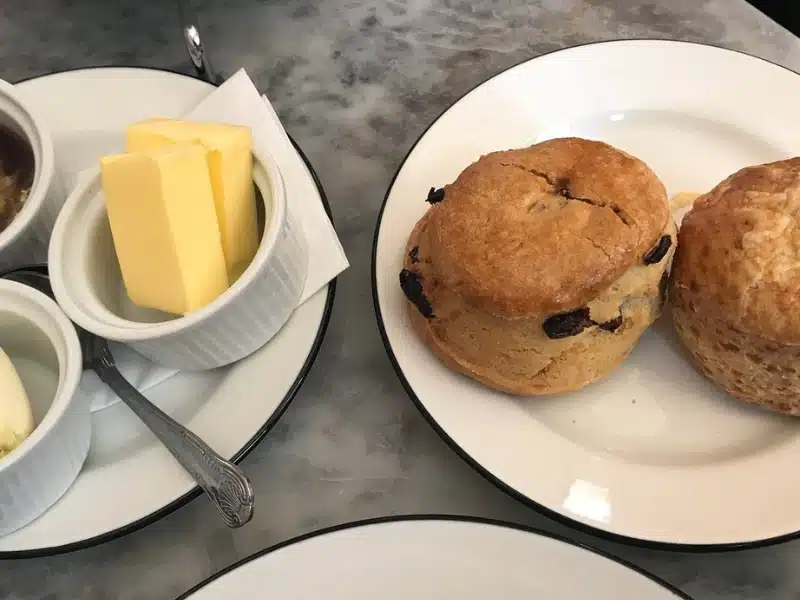 Scones on a plate on a marble table with pots of butter, jam and cream