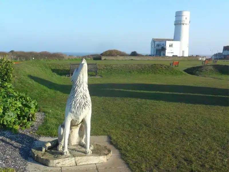 Wolf statue in front of a green with a white lighthouse in the background