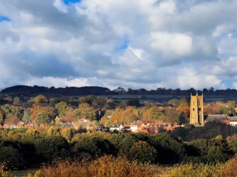English church tower from a distance surrounded by trees and houses