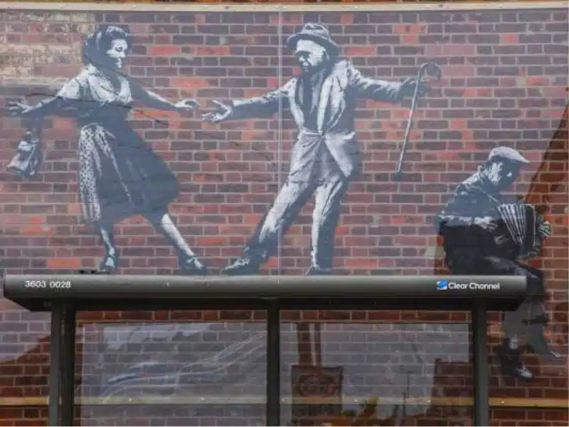 wall mural in black and white depicting people dancing behind perspex above a bus shelter