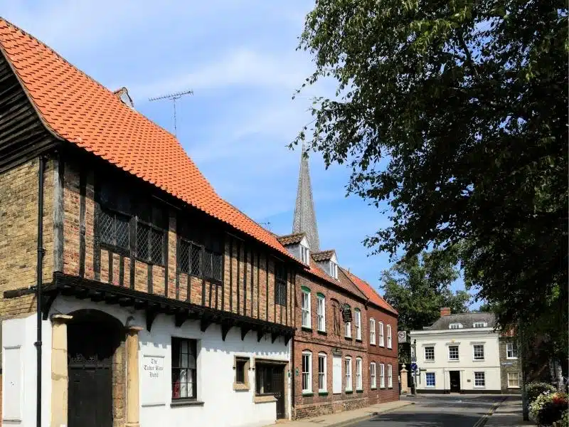 Historic buildings and half timbered house with a tree to the side and church spire in the background